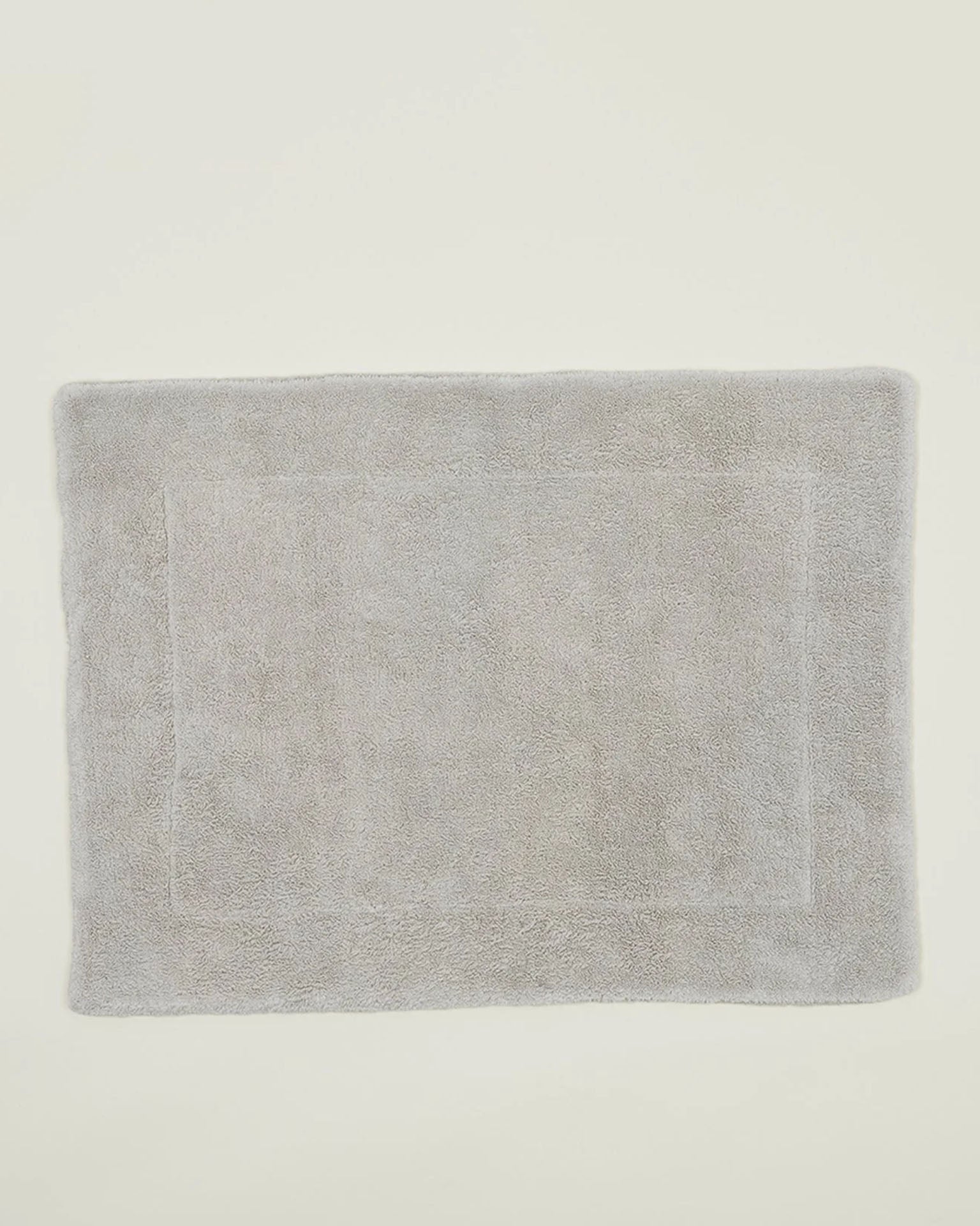 The Hawkins New York Simple Terry Bath Mat in Light Grey, made from soft cotton with a minimalist border, is featured on an off-white background.
