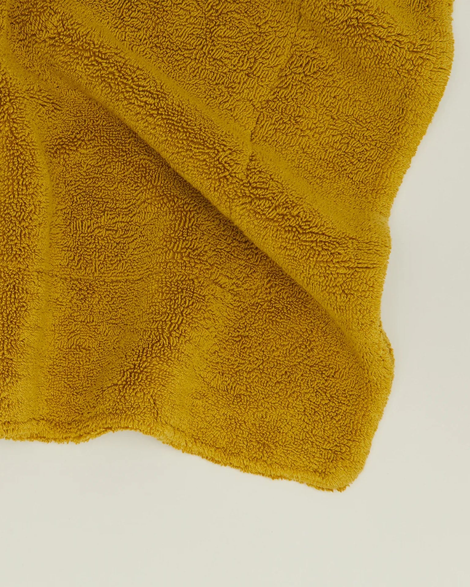 The Hawkins New York Simple Terry Bath Mat in Mustard is displayed spread out on a plain, light-colored surface.