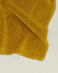 The Hawkins New York Simple Terry Bath Mat in Mustard is displayed spread out on a plain, light-colored surface.