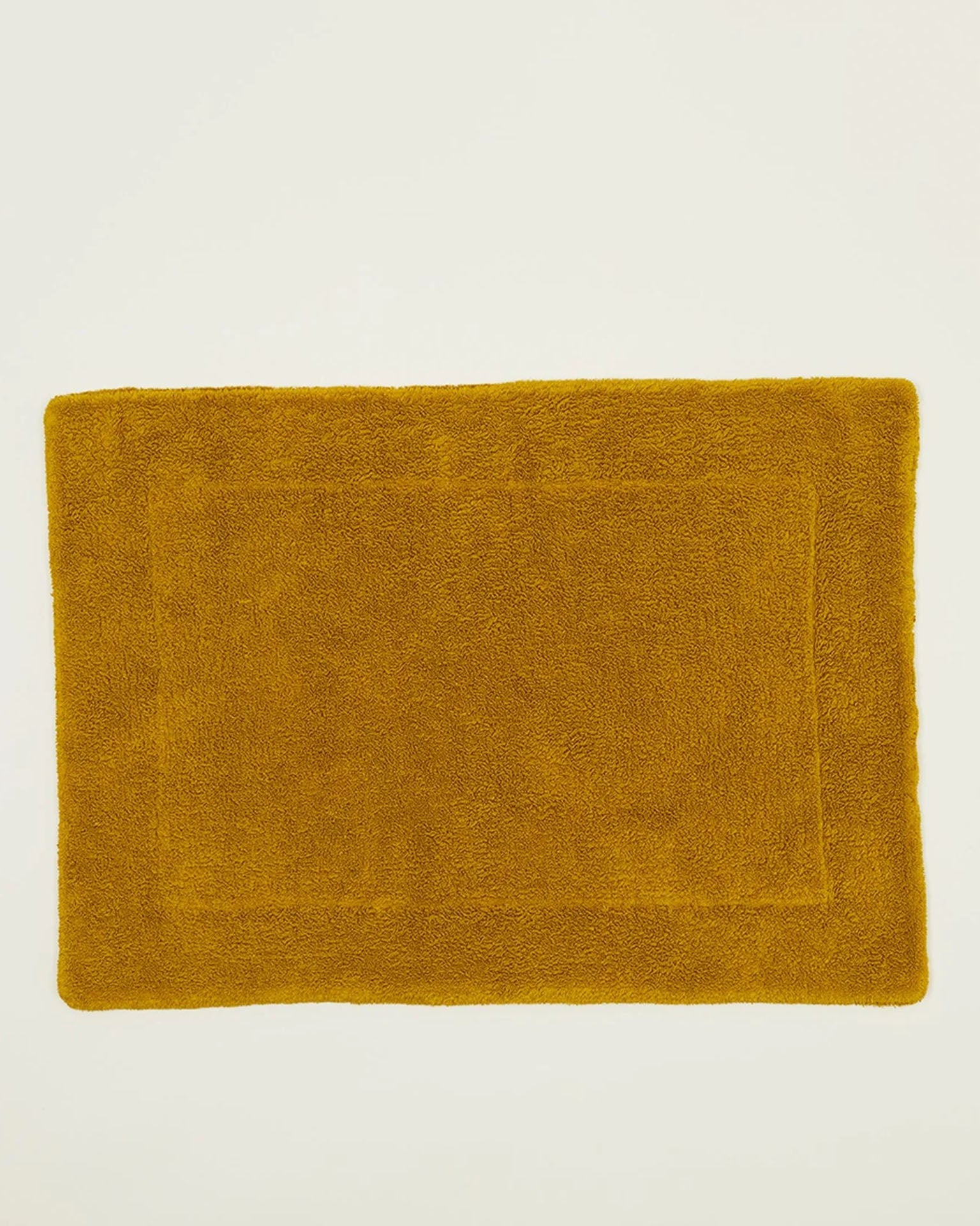 A Simple Terry Bath Mat in Mustard by Hawkins New York, crafted from soft cotton with a subtle border, is shown on a plain light background.