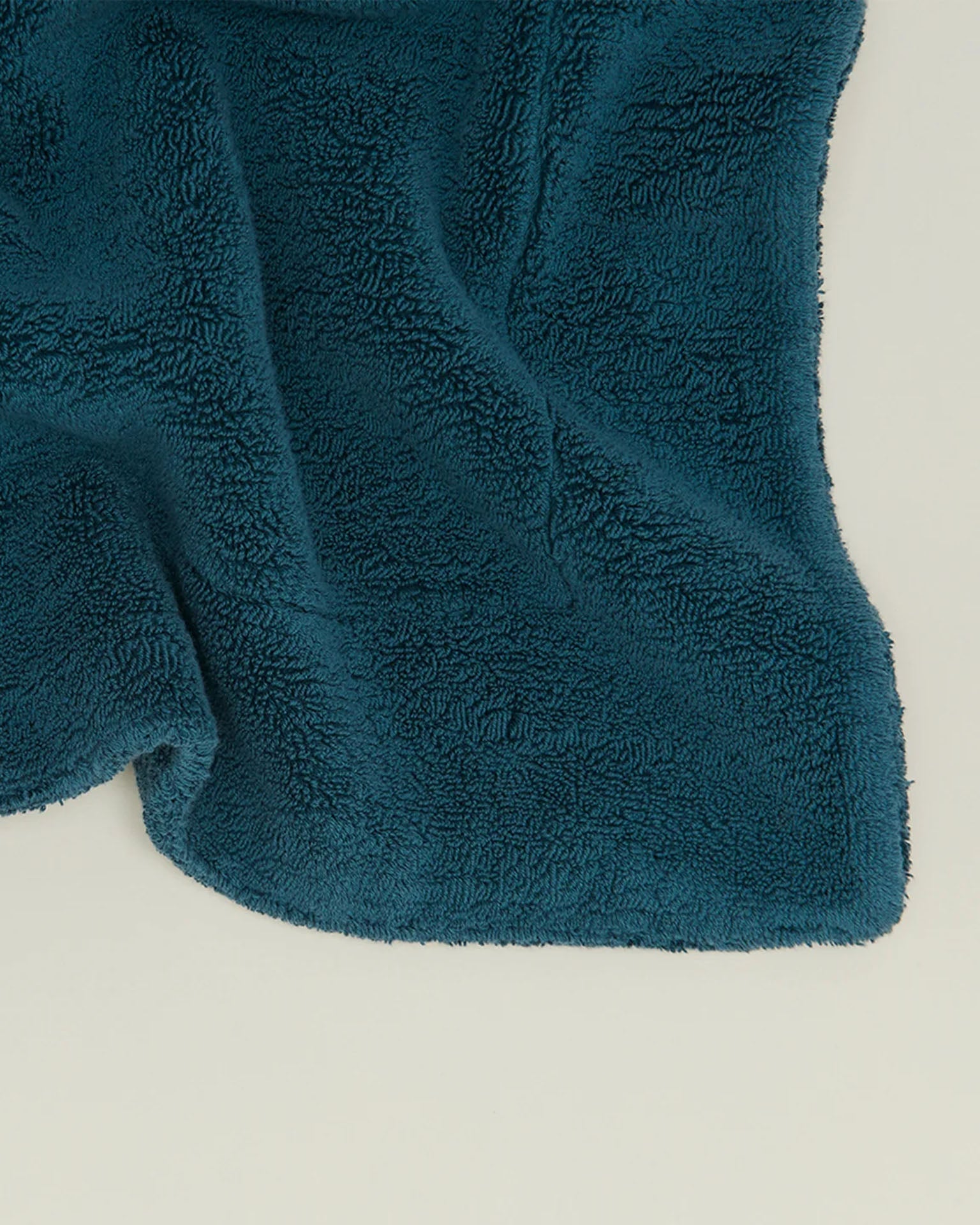 A close-up of the Simple Terry Bath Mat in Peacock by Hawkins New York, featuring dark teal textured cotton with curved edges, spread out on a light surface.