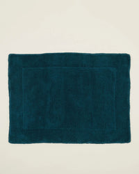 A rectangular Hawkins New York Simple Terry Bath Mat in Peacock, crafted from soft cotton with a textured border, is placed on a plain off-white background.