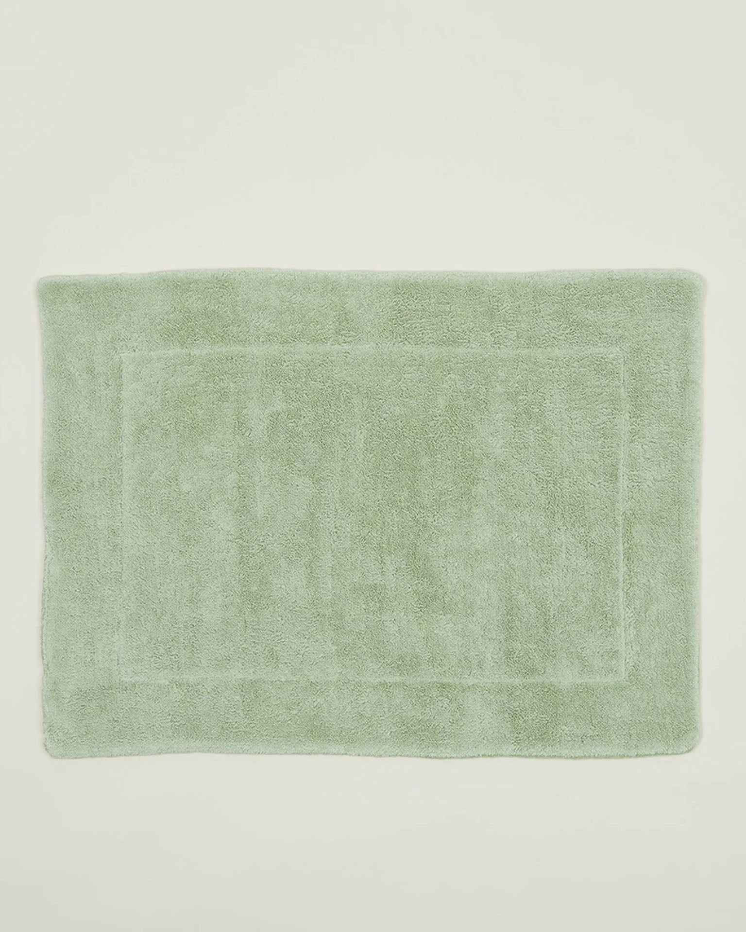 The Simple Terry Bath Mat in Sage by Hawkins New York is a rectangular, soft cotton bath mat with a subtle border design, shown on an off-white background.