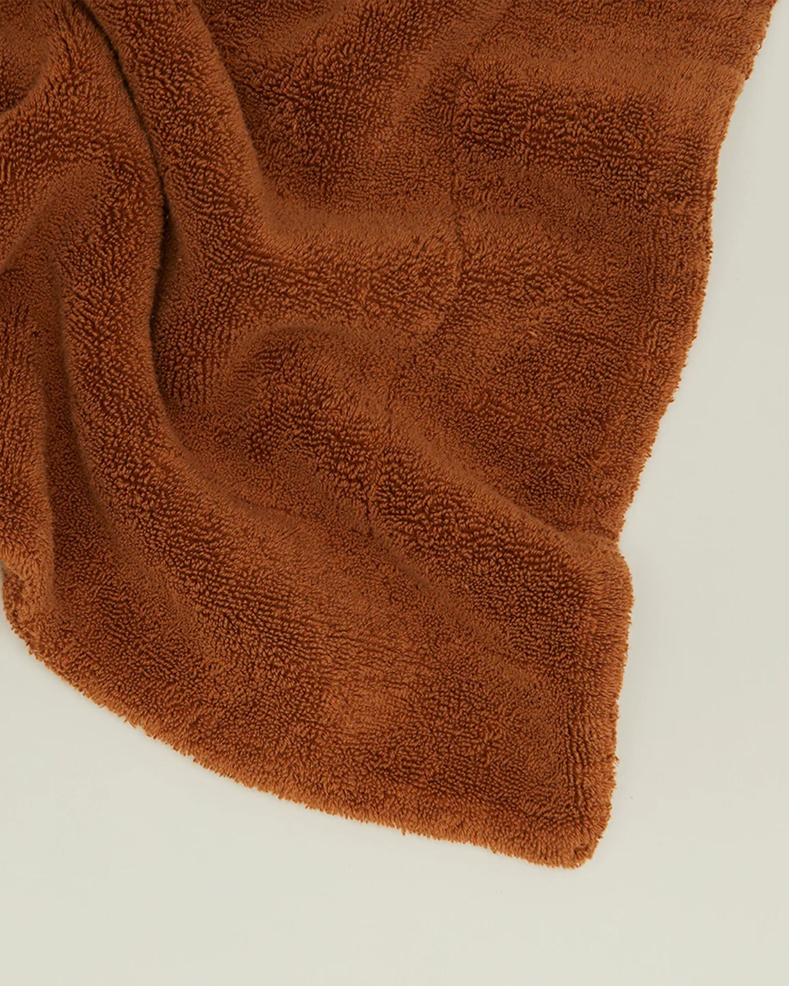 A soft, terracotta Simple Terry Bath Mat by Hawkins New York lies partially folded on a plain light surface.