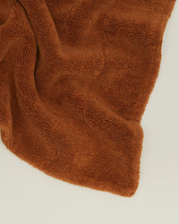 A soft, terracotta Simple Terry Bath Mat by Hawkins New York lies partially folded on a plain light surface.