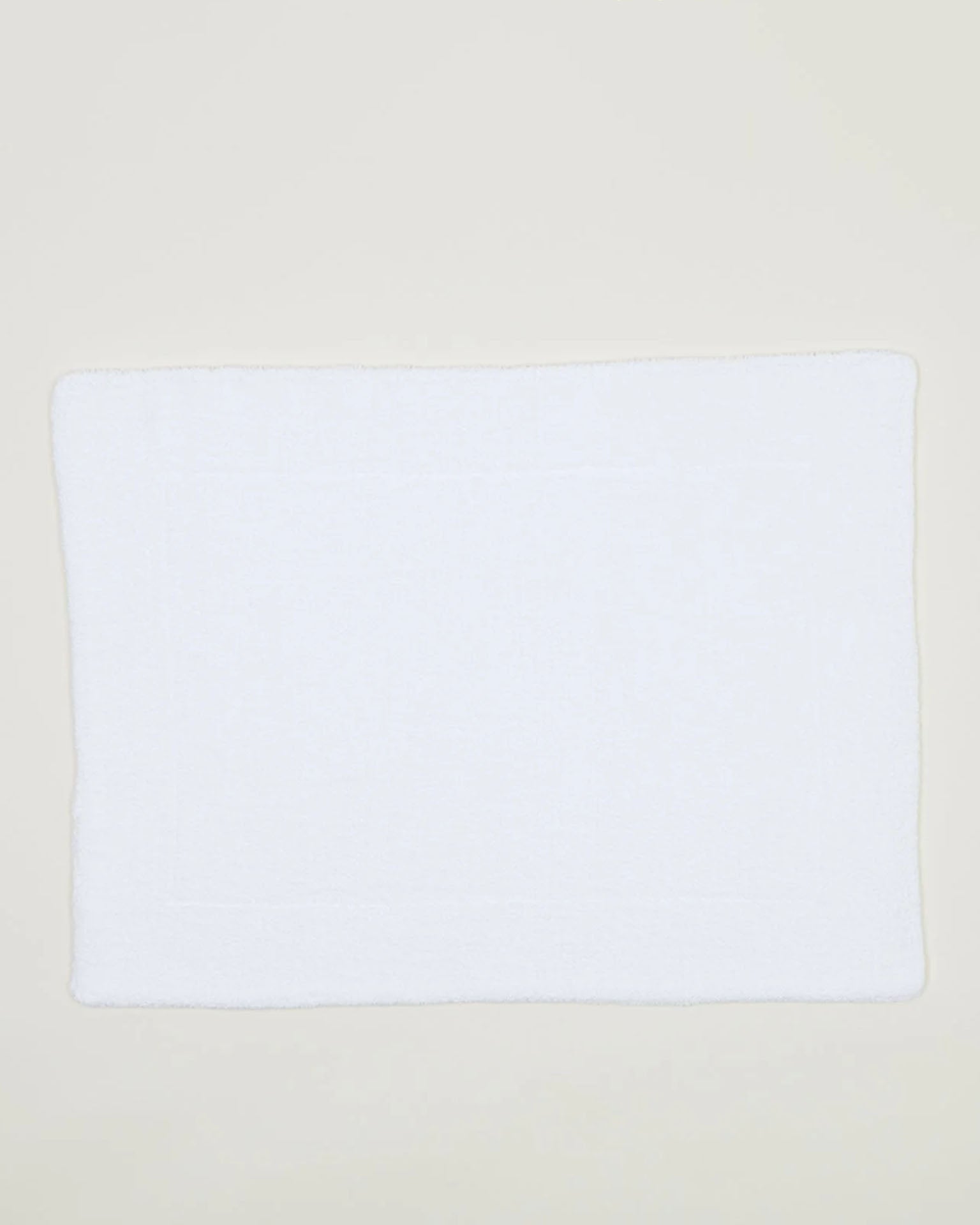 The Hawkins New York Simple Terry Bath Mat in White, crafted from cotton, is laid flat on a light-colored surface.