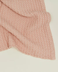 A close-up of the Simple Waffle Bath Sheet in Blush by Hawkins New York, featuring a soft, textured waffle-knit pattern and neatly folded on a light cream-colored surface.
