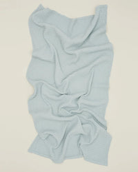 The Simple Waffle Bath Sheet in Sky by Hawkins New York, featuring a textured waffle-knit design in light blue, is laid out on an off-white surface with soft folds and natural wrinkles throughout the fabric.