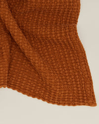 A close-up of the Simple Waffle Bath Sheet in Terracotta by Hawkins New York, made in Portugal, highlights its textured honeycomb pattern gently draped on a light background.