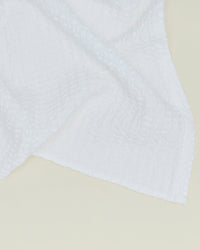 A close-up of the Hawkins New York Simple Waffle Bath Sheet in White, showing its textured grid pattern reminiscent of waffle towels, draped against a light beige background.