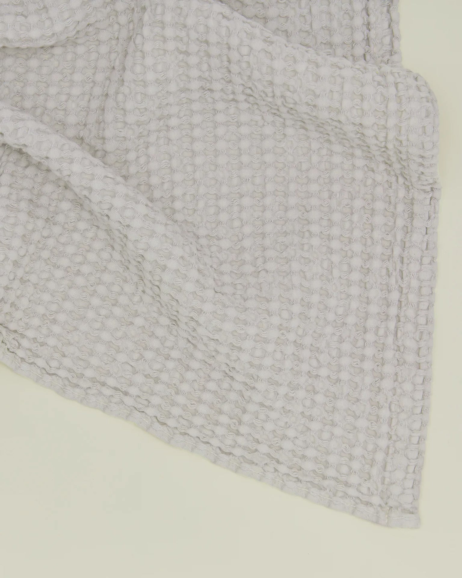 A close-up of the Simple Waffle Bath Towel in Light Grey by Hawkins New York showcases its textured, waffle-knit fabric and quality weave, ideal for highlighting the towels craftsmanship against a pale background.