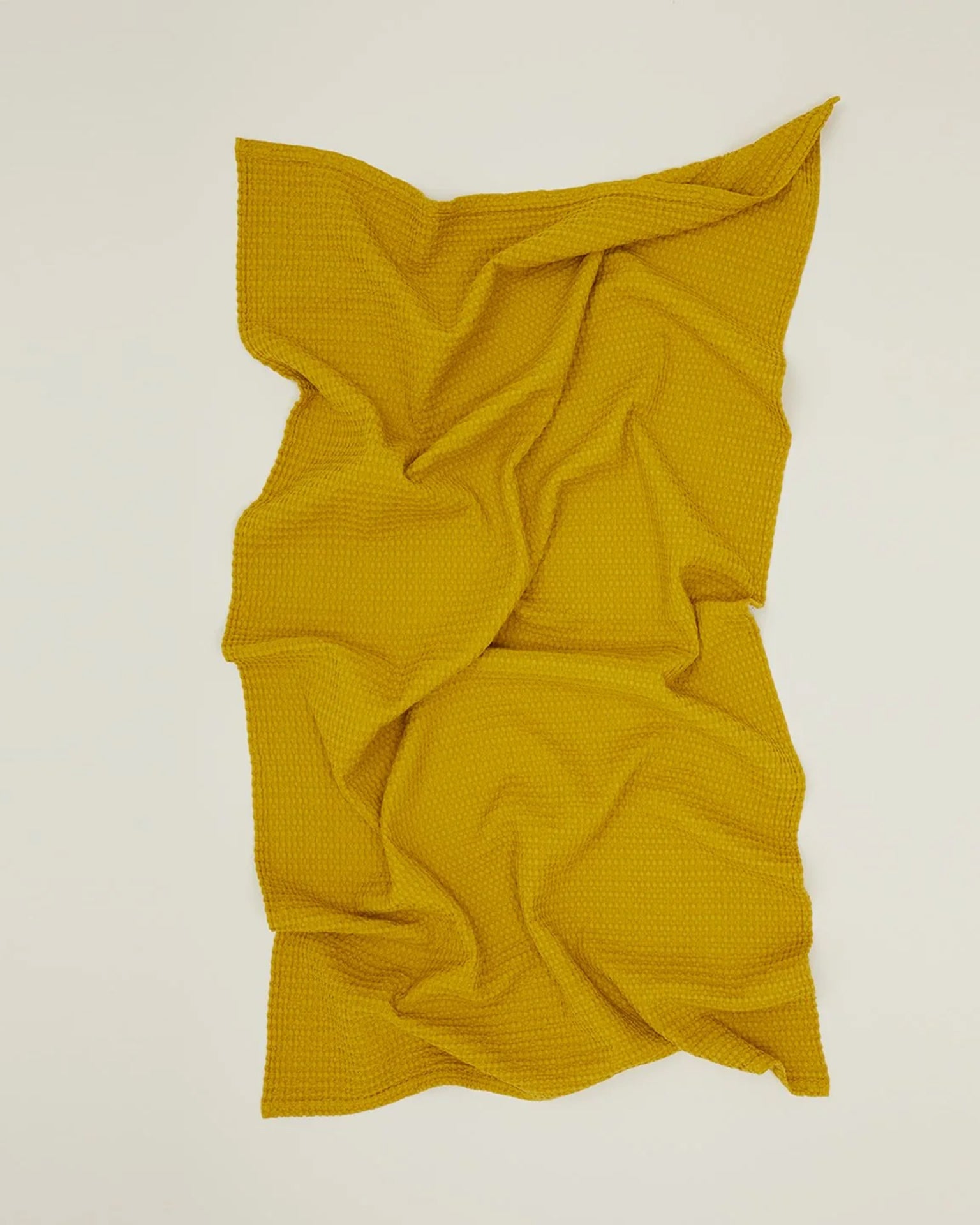 The Simple Waffle Bath Towel in Mustard by Hawkins New York, made of textured stonewashed cotton, is displayed on a flat, light surface with soft folds and creases.