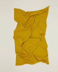 The Simple Waffle Bath Towel in Mustard by Hawkins New York, made of textured stonewashed cotton, is displayed on a flat, light surface with soft folds and creases.