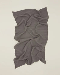 The Hawkins New York Simple Waffle Hand Towel in Dark Grey is laid flat on a light surface, displaying its textured waffle weave with soft folds and wrinkles.