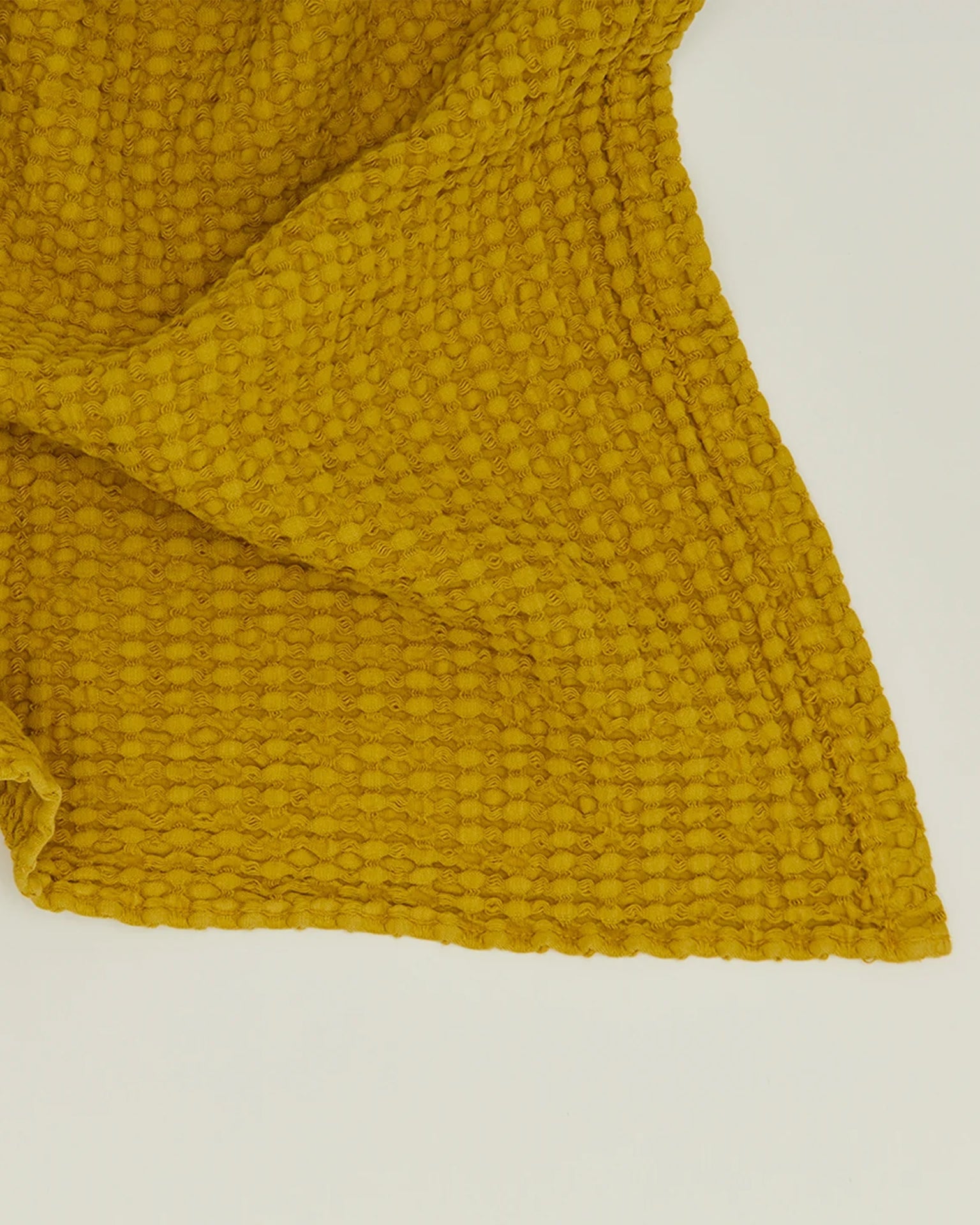 The Simple Waffle Hand Towel in Mustard by Hawkins New York, featuring a textured waffle-like pattern, is displayed on a plain white surface.