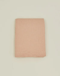 A folded, blush waffle-textured towel rests on a plain off-white background, evoking the delicate weave of the Hawkins New York Simple Waffle Shower Curtain.
