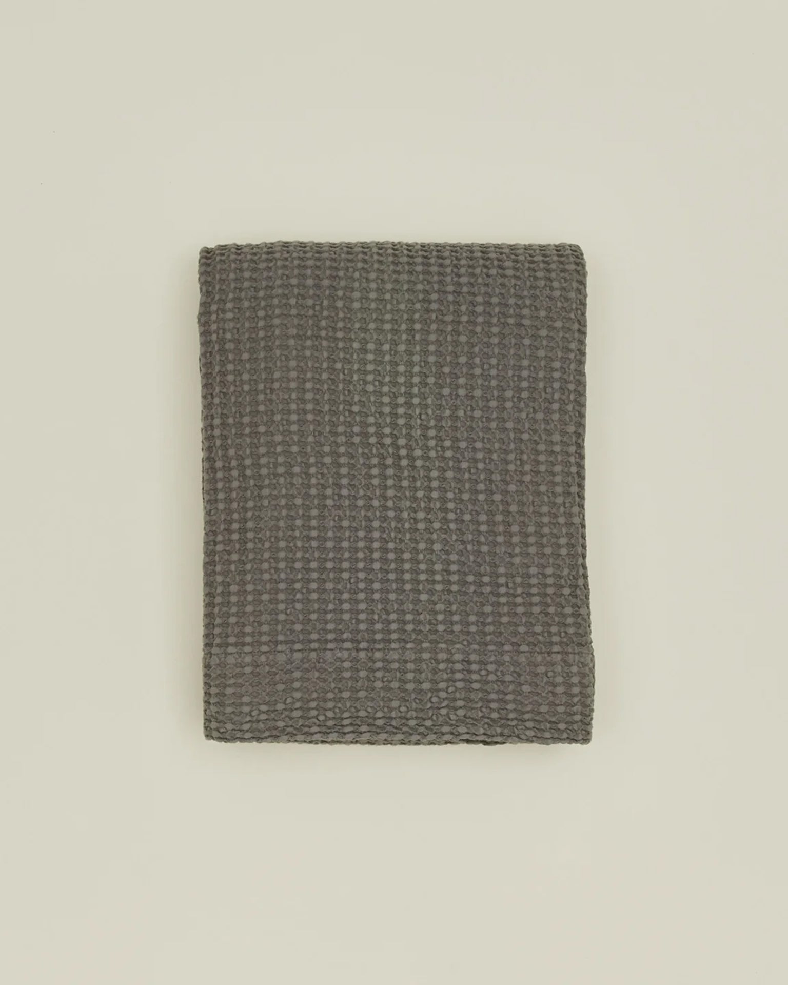 The Simple Waffle Shower Curtain in Dark Grey by Hawkins New York is displayed neatly folded on a plain light-colored surface.