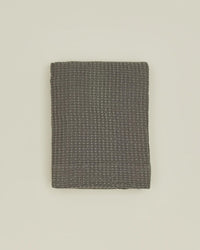 The Simple Waffle Shower Curtain in Dark Grey by Hawkins New York is displayed neatly folded on a plain light-colored surface.