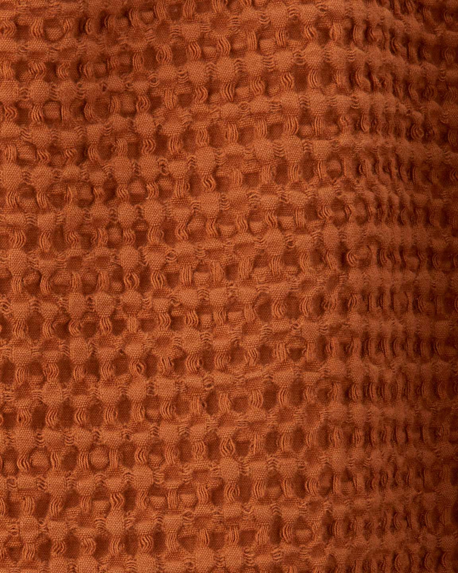 Close-up of the Simple Waffle Shower Curtain in Terracotta from Hawkins New York, showcasing its textured, raised pattern on reddish-brown cotton fabric.