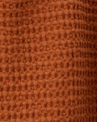 Close-up of the Simple Waffle Shower Curtain in Terracotta from Hawkins New York, showcasing its textured, raised pattern on reddish-brown cotton fabric.