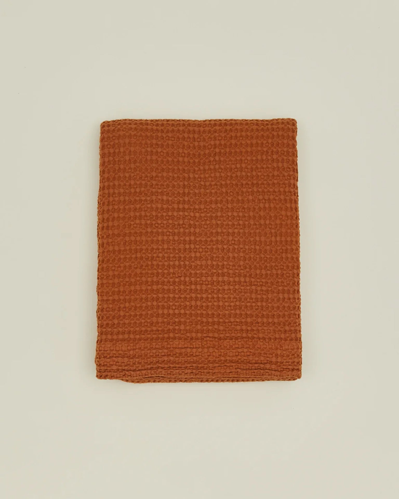A folded, textured terracotta towel is set on a plain off-white background, evoking the warm tones of the Hawkins New York Simple Waffle Shower Curtain in Terracotta.