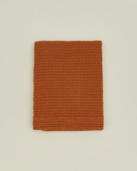 A folded, textured terracotta towel is set on a plain off-white background, evoking the warm tones of the Hawkins New York Simple Waffle Shower Curtain in Terracotta.