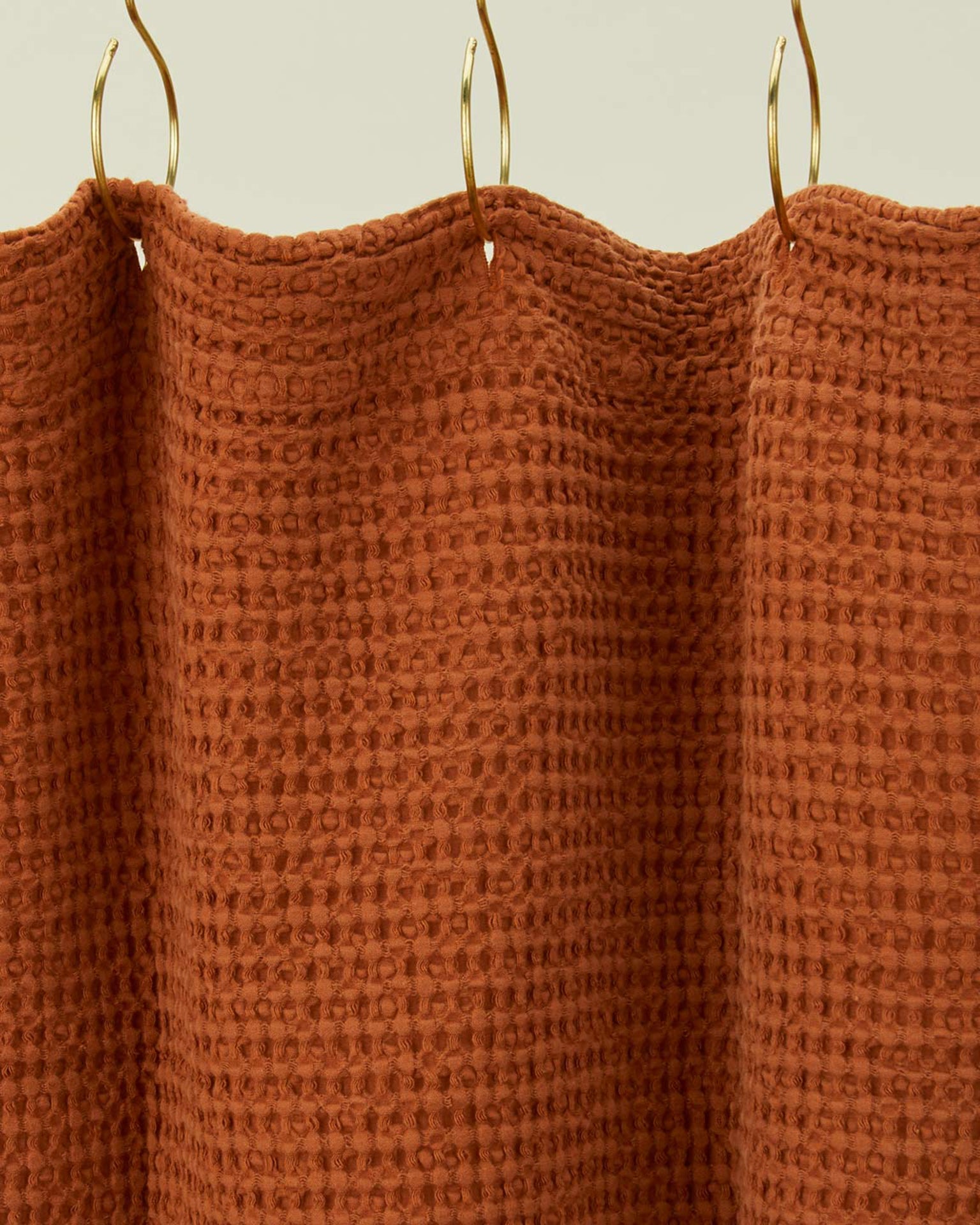 A close-up of the Simple Waffle Shower Curtain in Terracotta by Hawkins New York, featuring a textured design and hanging from gold hooks.