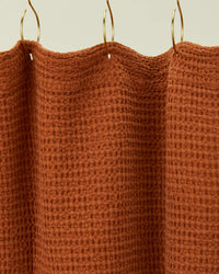A close-up of the Simple Waffle Shower Curtain in Terracotta by Hawkins New York, featuring a textured design and hanging from gold hooks.