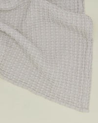 Close-up of the Simple Waffle Washcloth in Light Grey by Hawkins New York, featuring its textured waffle weave, corner, and edges on a pale surface.