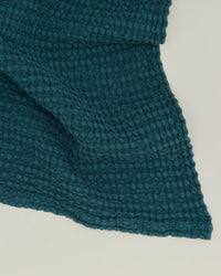 The Hawkins New York Simple Waffle Washcloth in Peacock, featuring a teal waffle weave texture, is shown folded on a light surface.