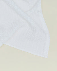 A close-up of the Simple Waffle Washcloth in White by Hawkins New York, featuring a textured waffle pattern and expertly crafted in Portugal, partially draped on a light-colored surface.