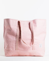 The Large East West Tote in Bubblegum by IMMODEST COTTON is an oversize light pink bag with two handles, a small white brand label on the bottom right, and a top button detail—perfect for everyday style and function.