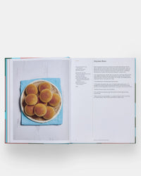 An open copy of The Spanish Mediterranean Islands Cookbook by Phaidon Press shows a photo of eight round buns on a plate atop a blue cloth and a recipe page titled Anytime Buns featuring Mediterranean instructions and ingredients.