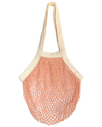 The French Market Bag No.2 in Ballet Pink by PILLOWPIA features beige handles and a peach-pink netted body, making it a stylish and reusable choice for shopping.
