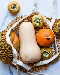 The PILLOWPIA French Market Bag No.2 in Goldenrod, filled with butternut squash, orange pumpkin, and persimmons, rests on a white marble surface.