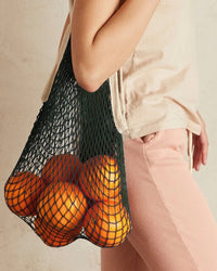 A person carries PILLOWPIAs The French Market Bag No.2 In Iron, filled with oranges, and wears a beige shirt with light pink pants.