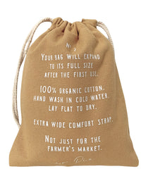 The French Market Bag No.2 in Wheat by PILLOWPIA is a tan organic cotton bag with white print, wide strap, and drawstring closure. Hand wash only—ideal for errands and outings beyond the farmers market.