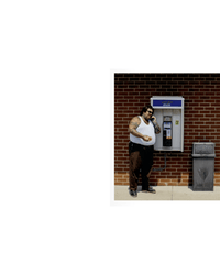 A man stands by a brick wall payphone on the sidewalk, holding Soups, Salads, Sandwiches from Random House, next to a trash can.