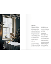 A softly lit room with a table draped in white, vases of dried flowers, and a big window; the right page features text about unique kitchens and The deVOL Kitchen by Random House.