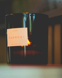 A Le Grand Marmont candle by ROEN, in black glass, glows with a visible flame on a flat surface, offering luxury fragrance from its premium coconut soy wax blend.