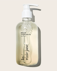 A clear pump bottle labeled Rosie Jane holds Dulce Everyday Body Wash, a light yellow hydrating vanilla cleanser. The bottle casts a soft shadow on a neutral background.
