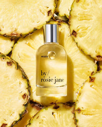 A bottle of Eau De Parfume in Missy by Rosie Jane sits on overlapping pineapple slices, capturing the lively essence of a tropical scent.