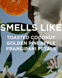 A close-up of an orange slice, cracked coconut, green leaves, and frangipani flowers against a blue background. Text: SMELLS LIKE TOASTED COCONUT, GOLDEN PINEAPPLE, FRANGIPANI PETALS—perfect for Rosie Jane Missy Everyday Body Oil.