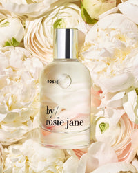A Rosie Jane Eau De Parfume in Rosie bottle rests among white and pale pink flowers, evoking a soft white musk fragrance and a delicate skin scent.