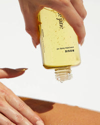 A hand pours Rosie Janes Rosie Everyday Body Oil from a clear bottle onto a forearm against a white background, highlighting the nourishing benefits of this hydrating body oil.