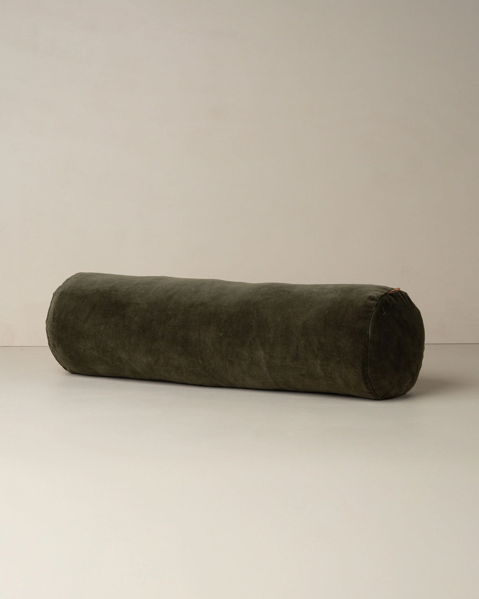 The Saarde Velvet Structured Bolster in Dark Olive rests on a plain, light surface against a neutral wall.