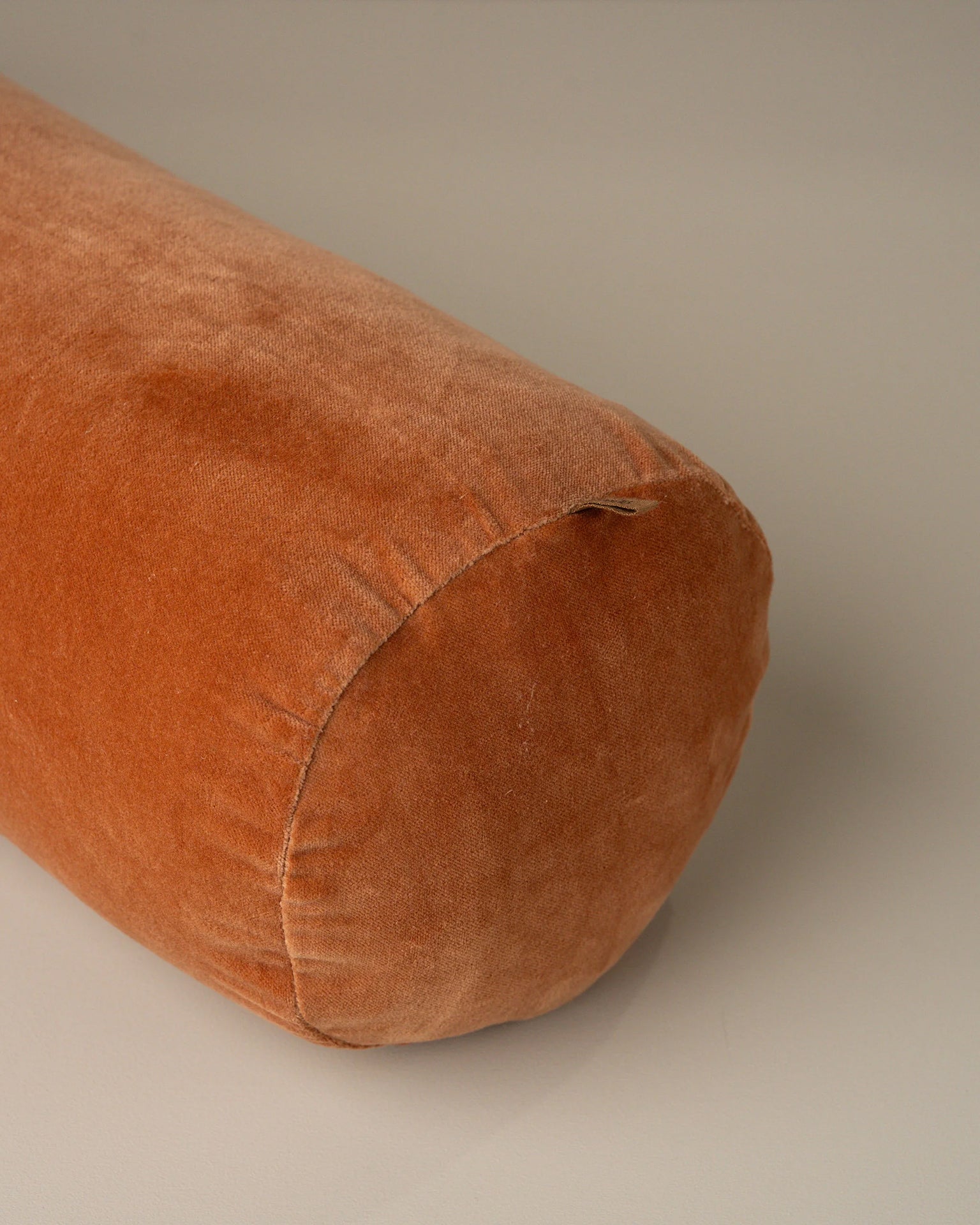 A close-up of the Saarde Velvet Structured Bolster in Terracotta, featuring a round design and plush velvet texture, set against a neutral background.