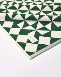 A close-up of the Gatsby Bath Mat in Sequoia by Slowtide, featuring a green and white geometric pattern on ultra-soft, sustainably sourced cotton, with a small Slowtide tag on the corner.
