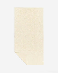 The Ginny Bath Towel by Slowtide is a beige, rectangular towel made from sustainably sourced cotton with a subtle animal print. Shown flat with a folded corner, it adds spa-like comfort and elegance to your bath routine.