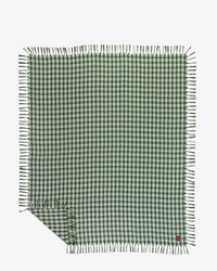 The Palaka L/W Beach Blanket in Sequoia by Slowtide features green and white checks with fringe edges, displayed flat with one corner slightly folded over.